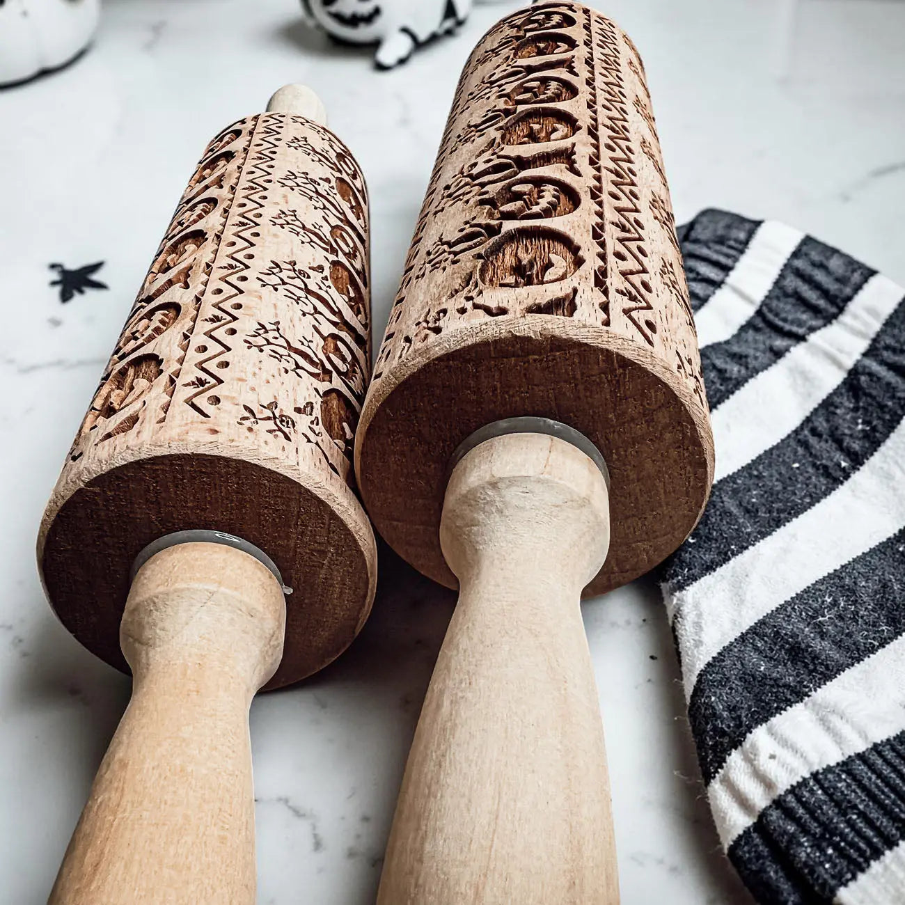 Two wooden embossing rolling pins with intricate patterns on a marble surface.