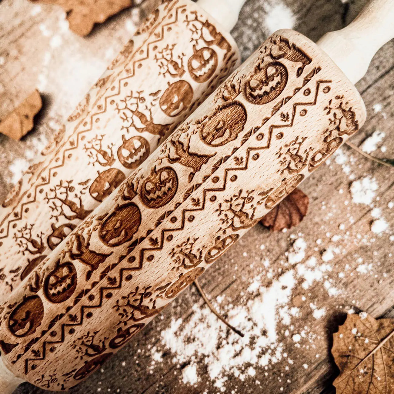 Two wooden embossing rolling pins with Halloween-themed patterns on a wooden surface with flour.