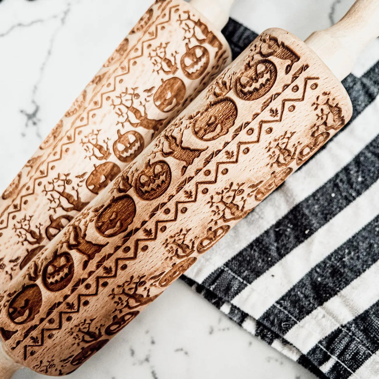 Two wooden rolling pins with embossed patterns on a marble surface.