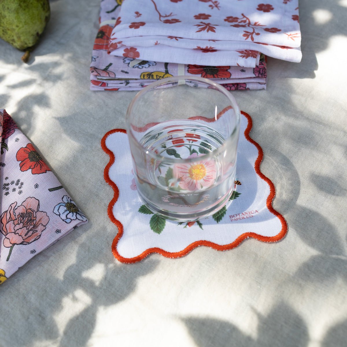 Glass with floral design on a matching coaster, surrounded by floral-patterned napkins on a textured surface.