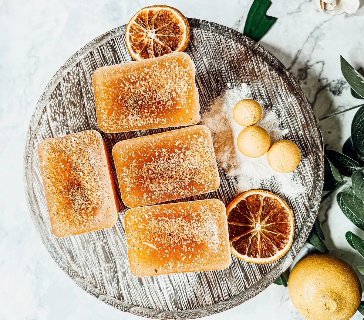 Orange-scented candles on a wooden tray with dried oranges and green leaves.