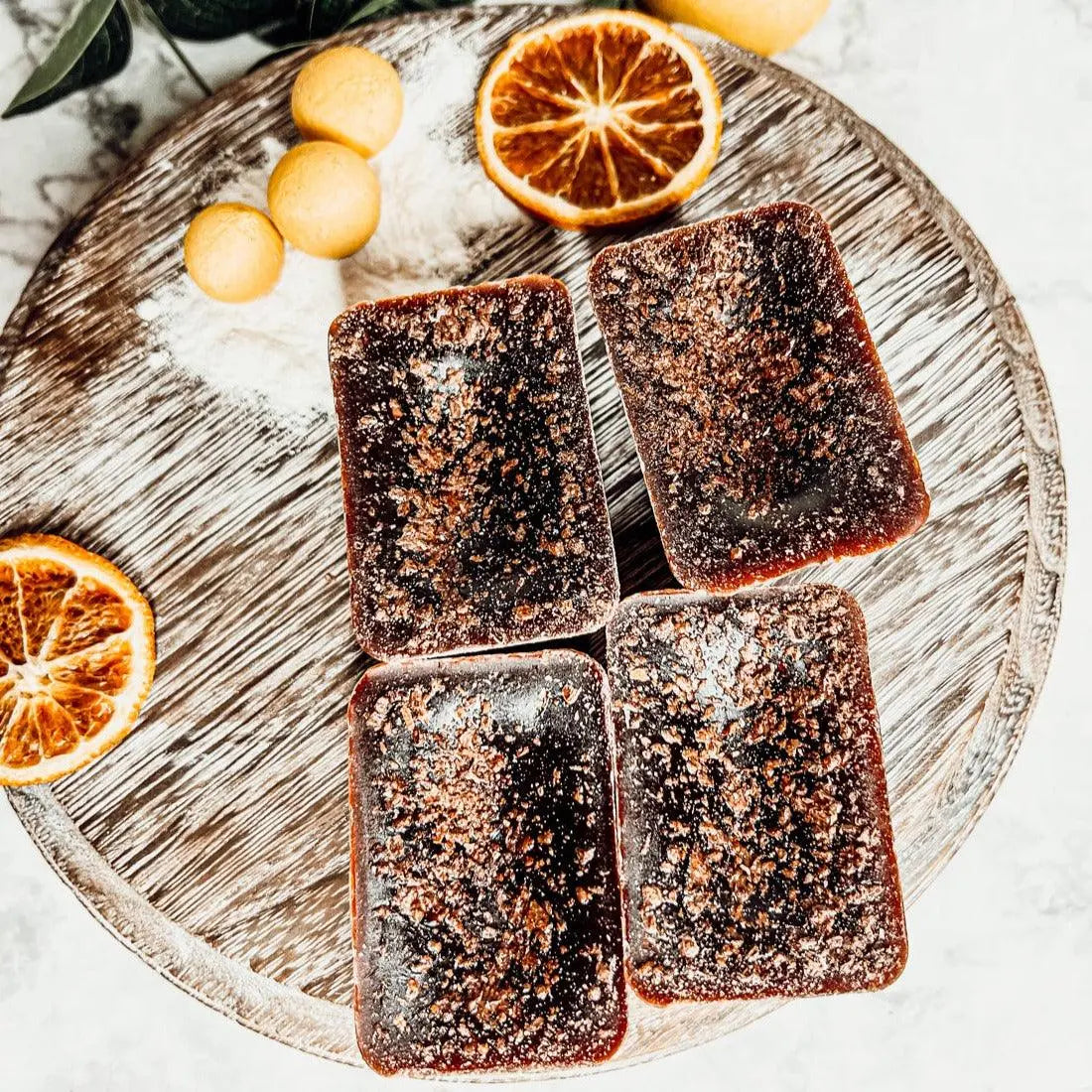 Four square brownies on a round wooden board with dried oranges and lemons.