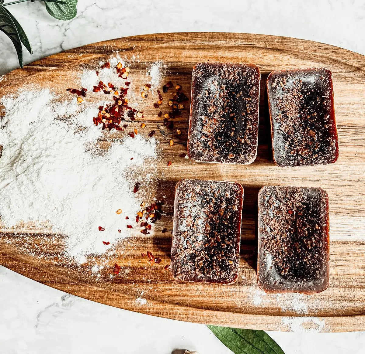 Four dark brown rectangular pastries on a wooden board with salt and red pepper flakes.