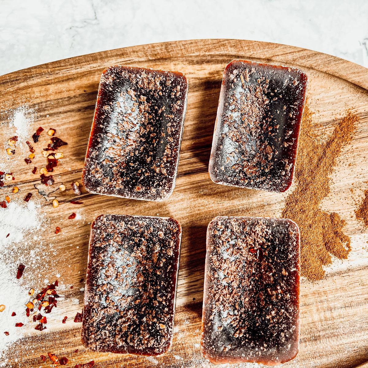 Four square pieces of seasoned meat on a wooden cutting board with spices around.