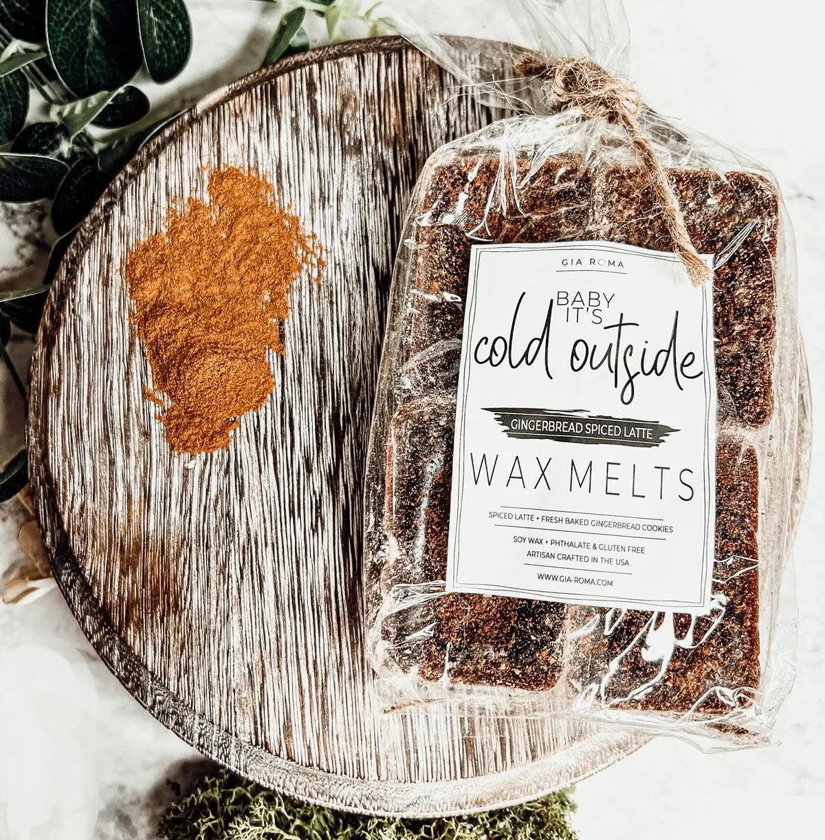 Packaged wax melts labeled 'Baby It's Cold Outside' on a wooden surface with decorative elements.