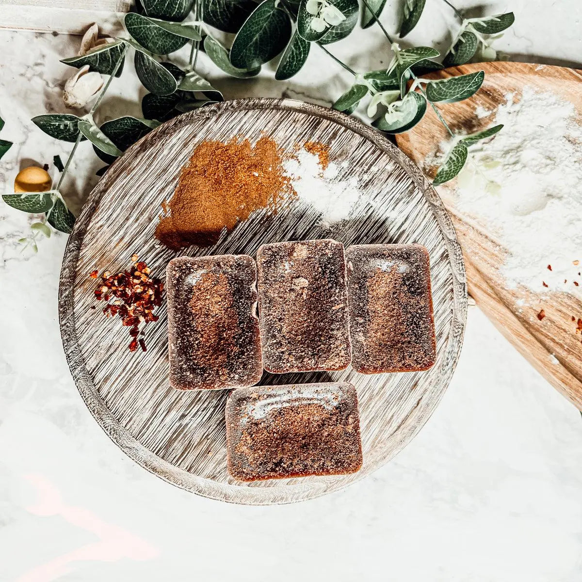 Wooden board with sliced brownies, spices, and greenery on a light background