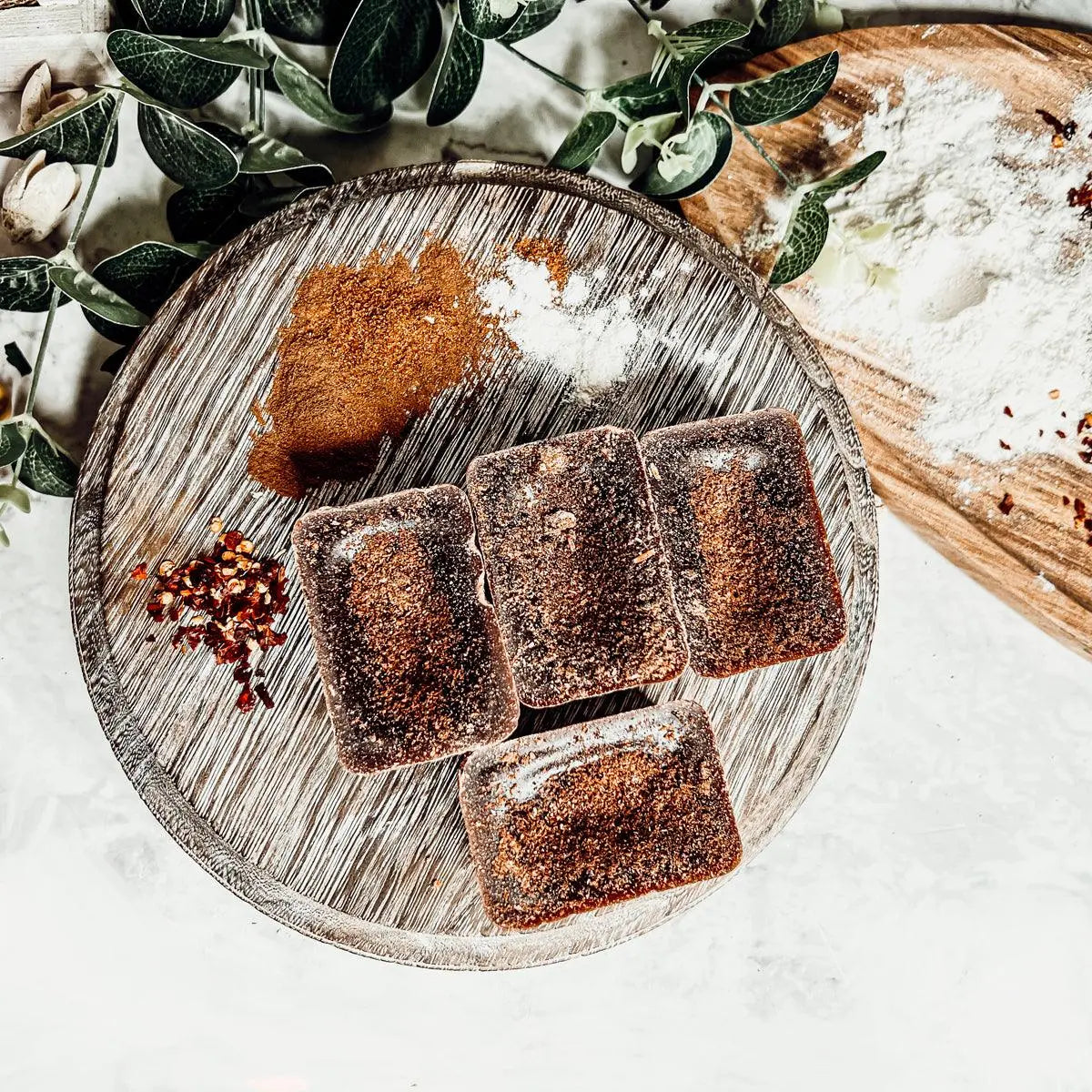 Square brownies on a wooden plate with greenery and flour in the background
