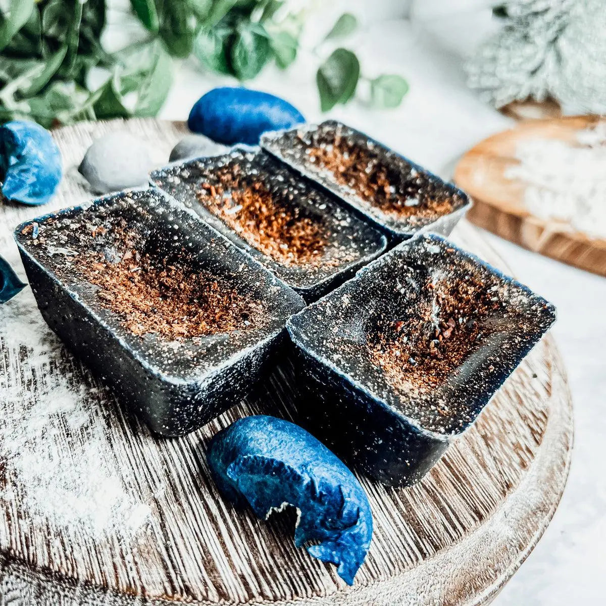 Blue and brown soap bars on a wooden surface with greenery in the background