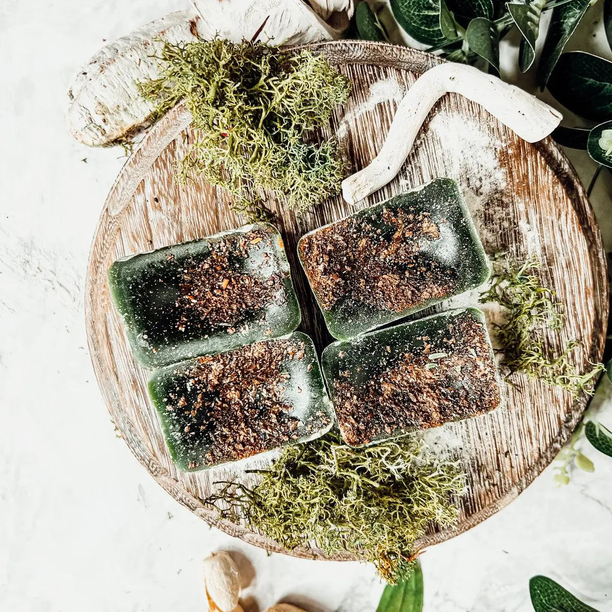 Four green soap bars on a wooden board with greenery around