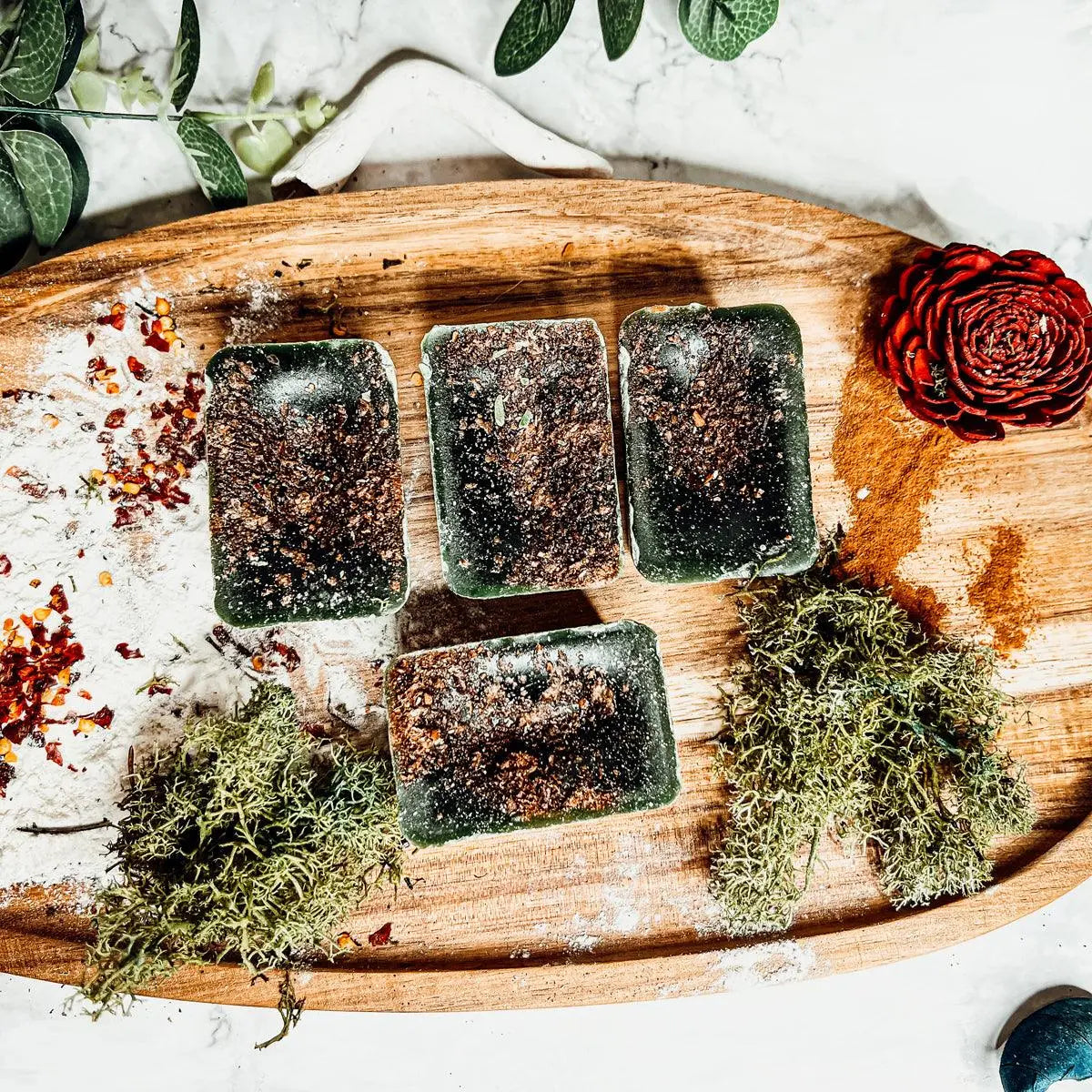 Five green soap bars on a wooden board with decorative elements