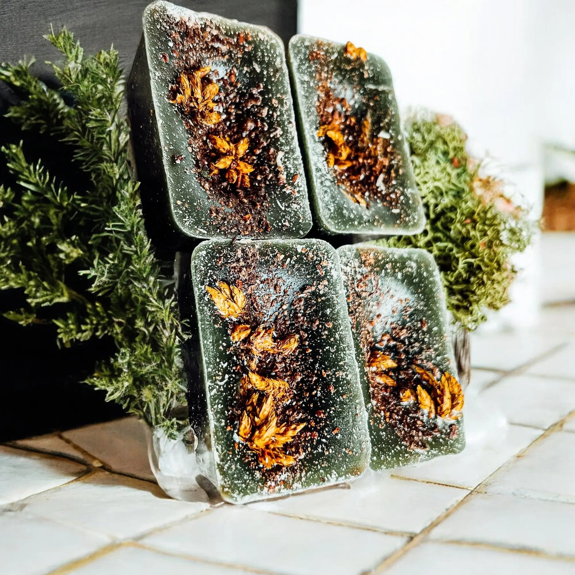 Four rectangular soap bars with natural ingredients on a tiled surface.