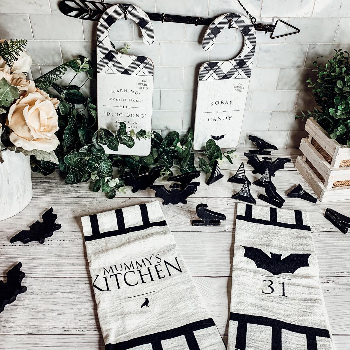 Halloween-themed kitchen decor items including signs and towels on a wooden surface.