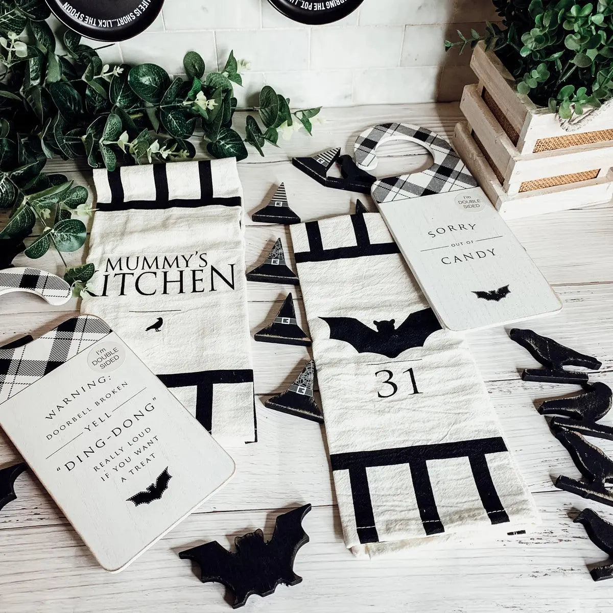 Halloween-themed kitchen towels with bat designs and text on a wooden surface.