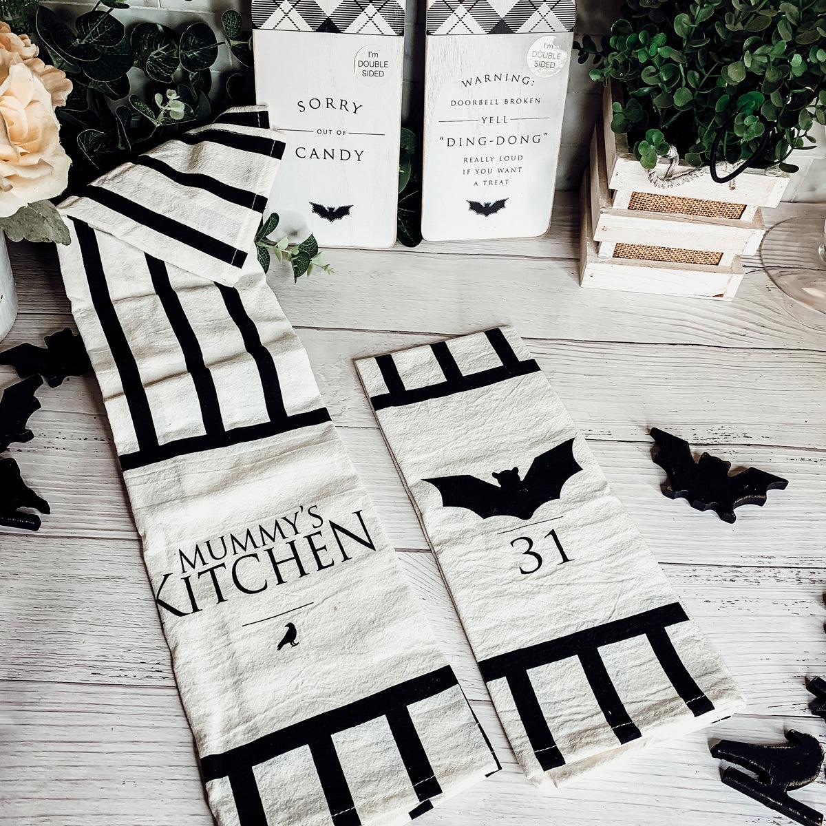 Halloween-themed kitchen towels with bat designs on a wooden surface.