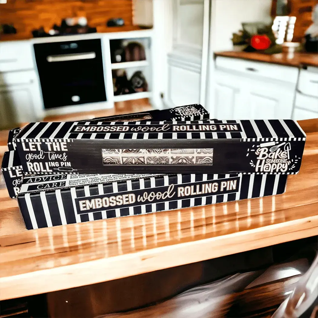 Two embossed wood rolling pins in packaging on a kitchen counter.