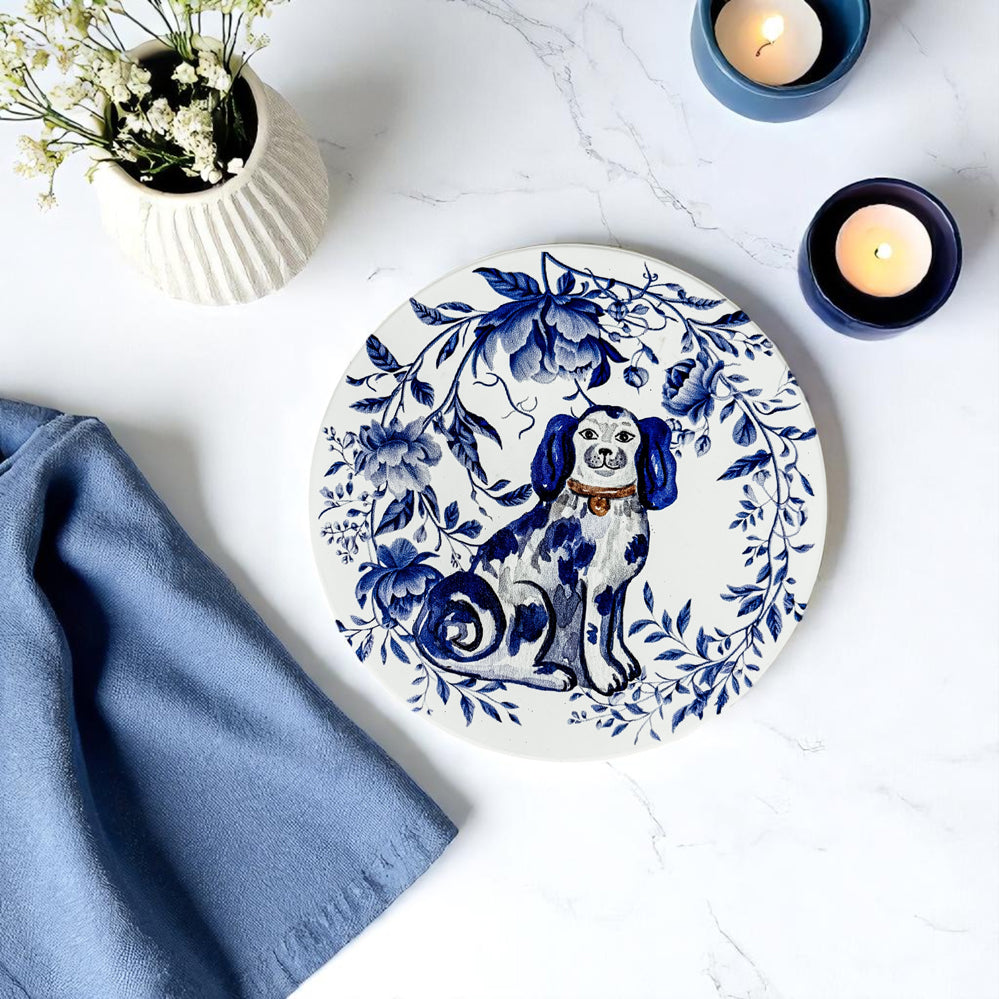 Round ceramic coaster with a blue and white dog design on a marble surface with candles and flowers.
