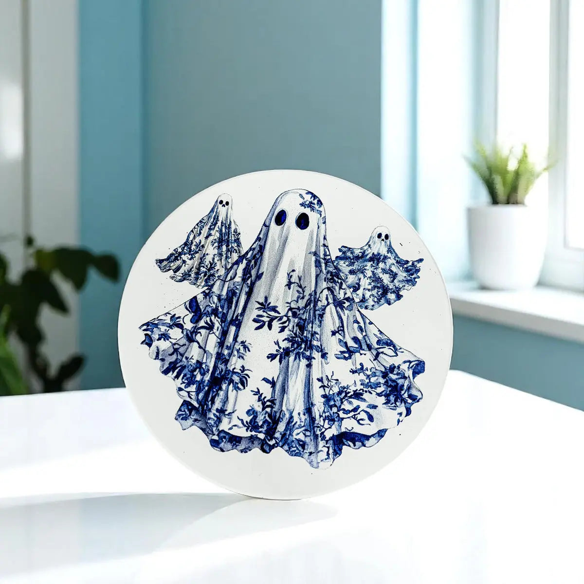 Round white coaster with blue floral ghost design on a light surface.