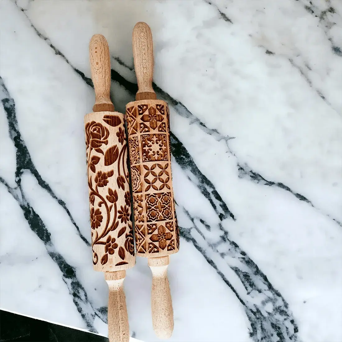 Two wooden rolling pins with embossed patterns on a marble surface