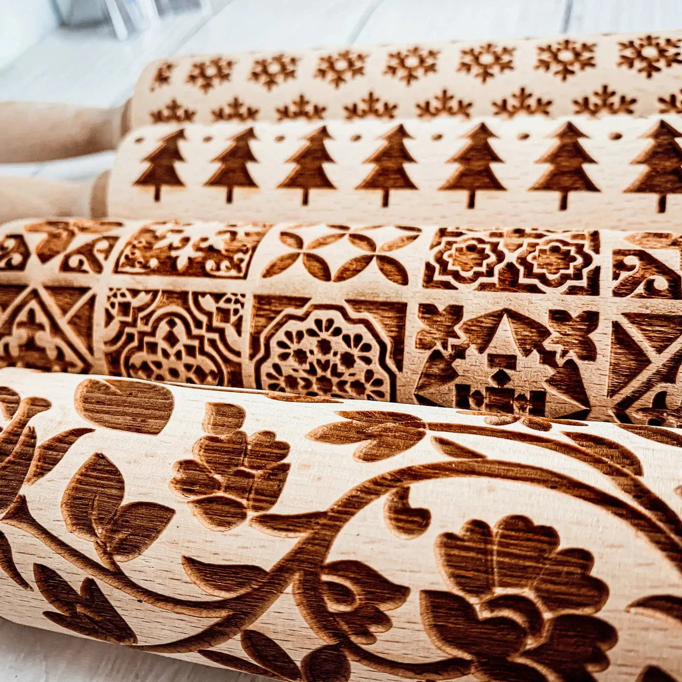 Three wooden rolling pins with engraved patterns on a light background