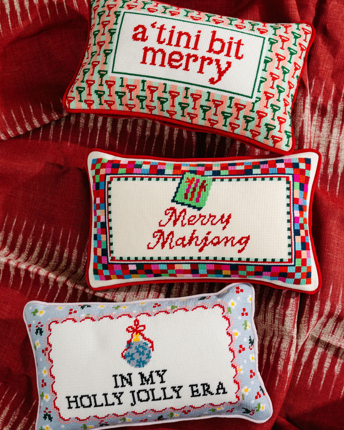 Three decorative pillows with festive sayings on a red fabric background