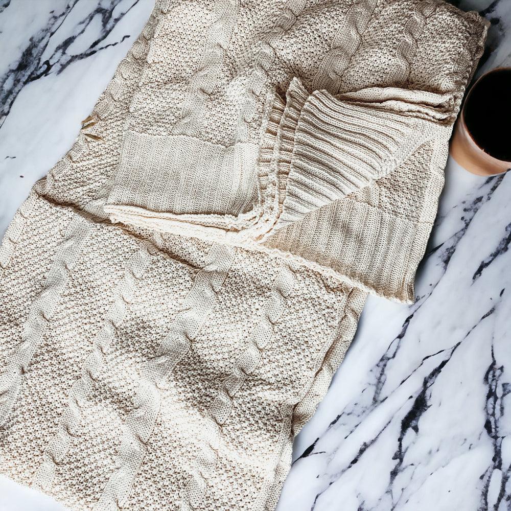 Cozy cream cable knit blanket on marble surface with coffee mug, farmhouse decor