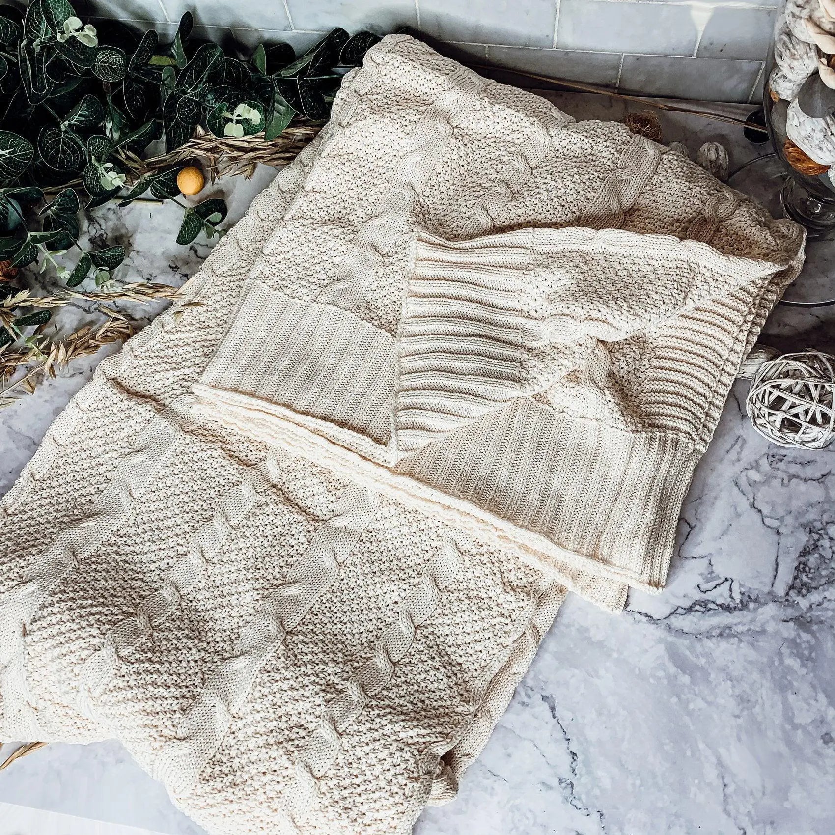 Cozy cream cable knit blanket on marble surface with greenery and rustic decor accents