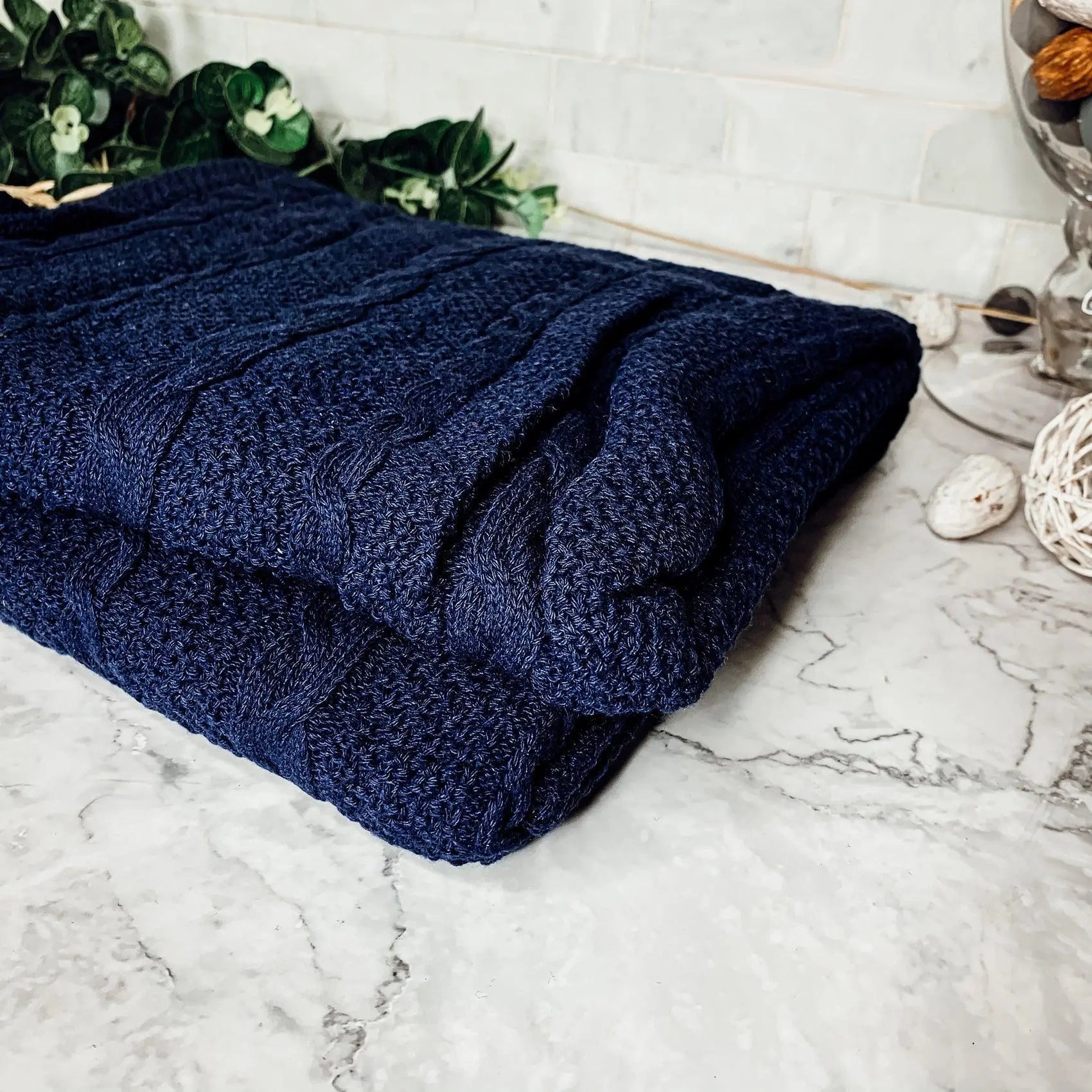 Navy blue cable knit throw blanket on marble surface, cozy farmhouse decor