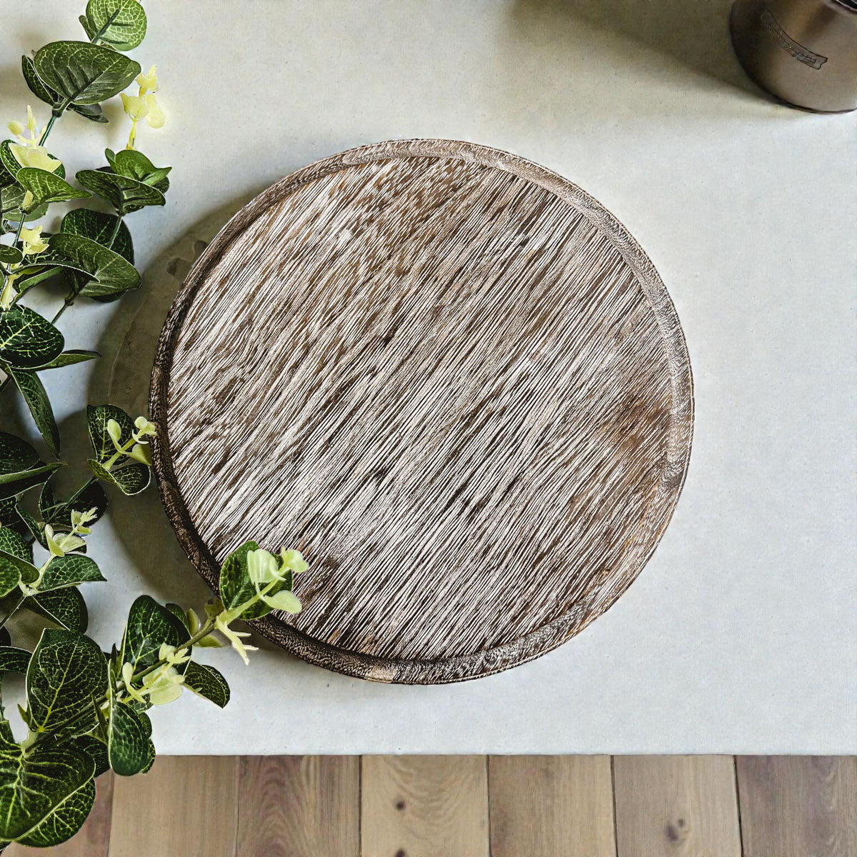 Round wooden cutting board on a light surface with greenery
