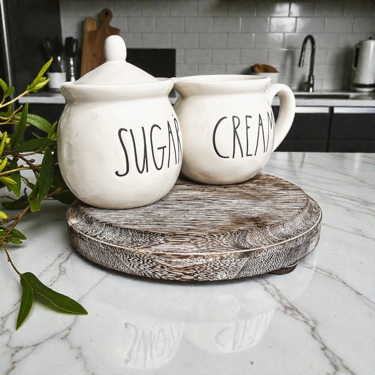 Two white ceramic jars labeled 'Sugar' and 'Cream' on a wooden stand in a kitchen.
