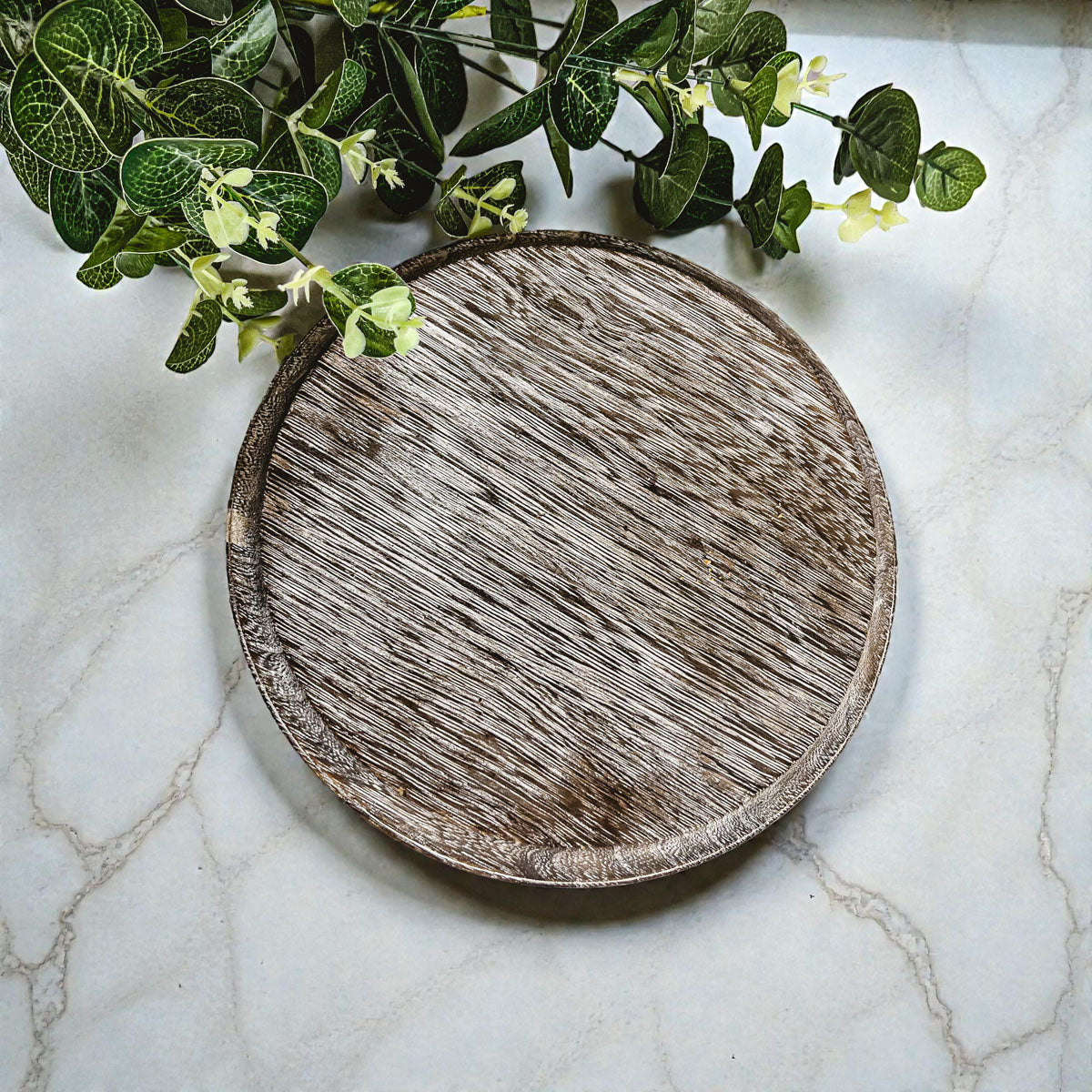 Round wooden tray on a marble surface with green leaves in the corner