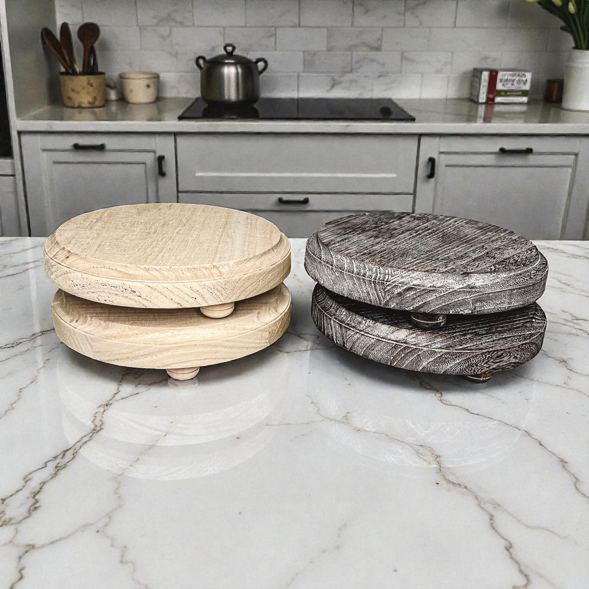 Two wooden coasters, one light wood and one dark wood, on a marble countertop with a kitchen background.