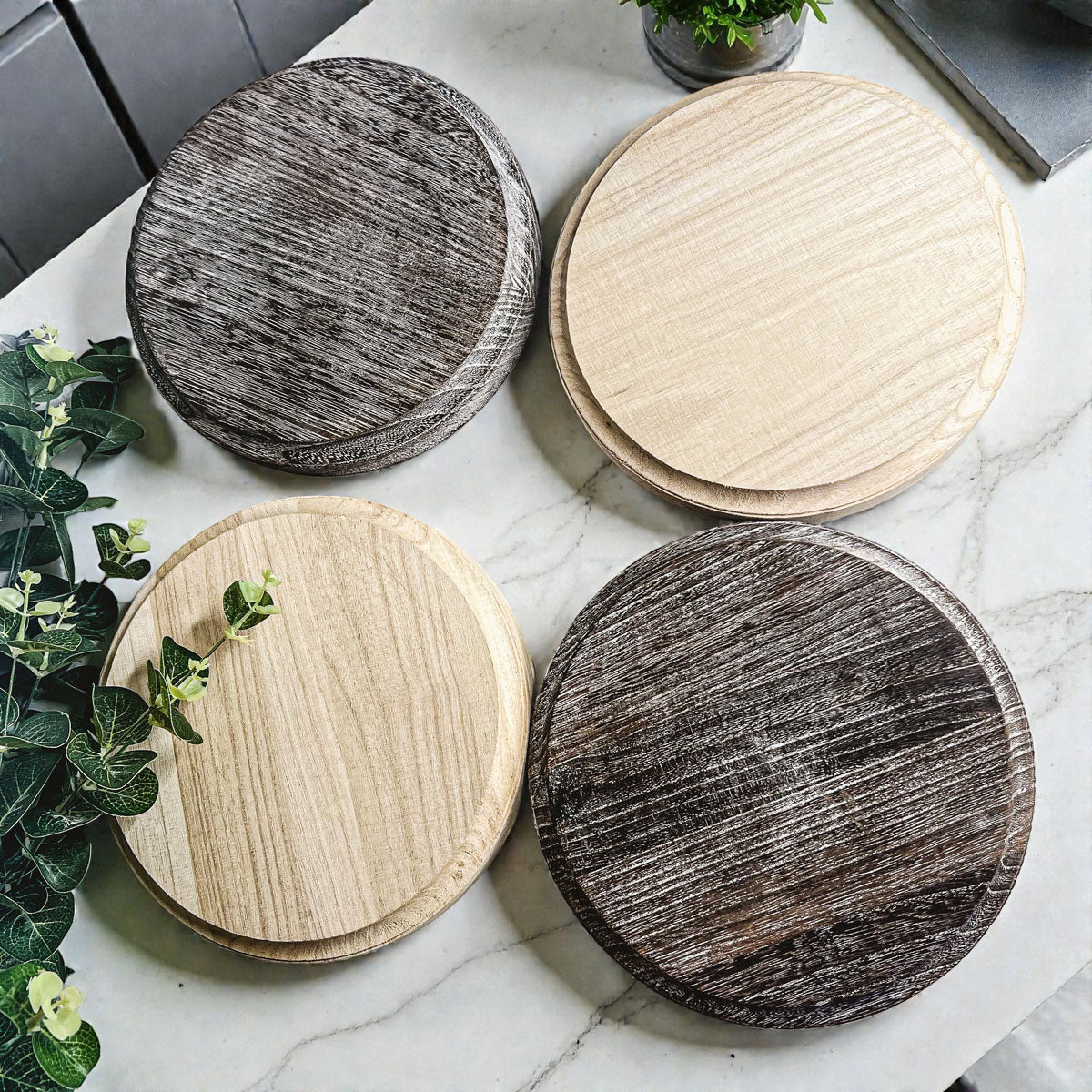 Four round wooden coasters on a marble surface with plants around.