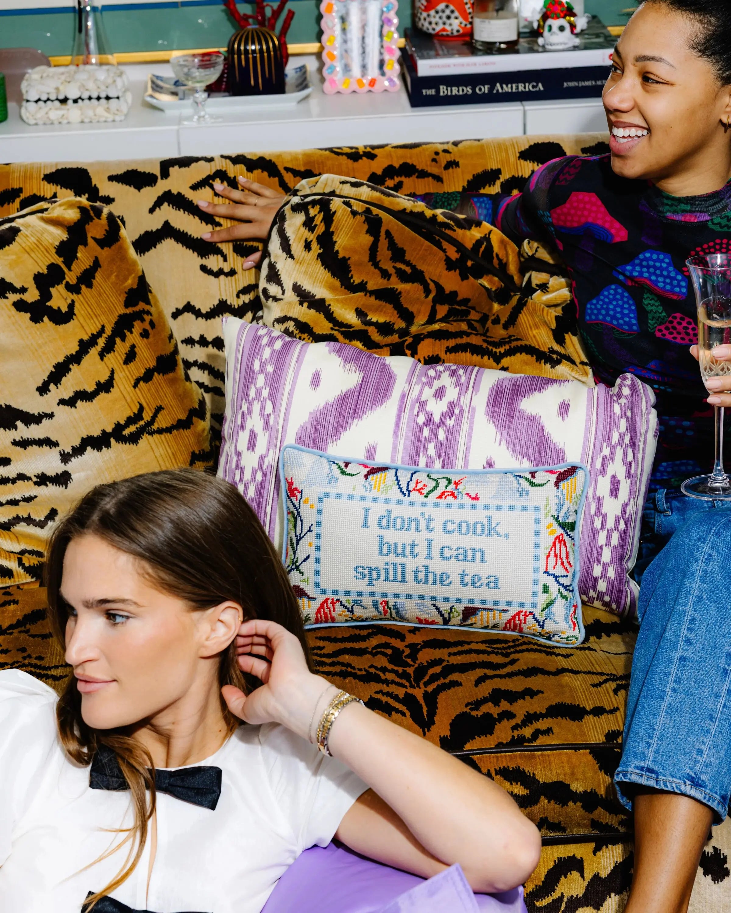 Two women sitting on a tiger-patterned couch with decorative pillows.