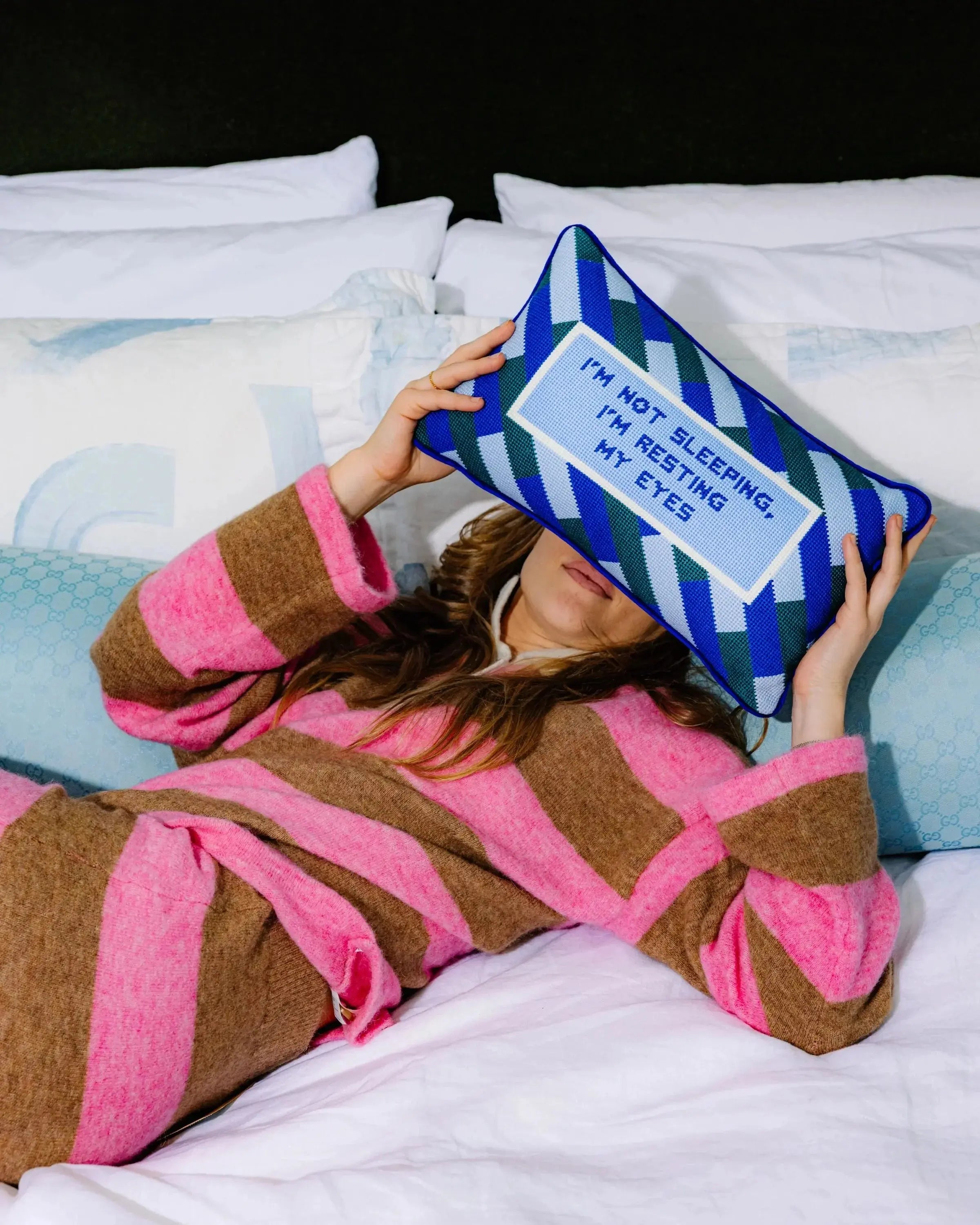 Person in a robe holding a pillow with text on it, lying on a bed.
