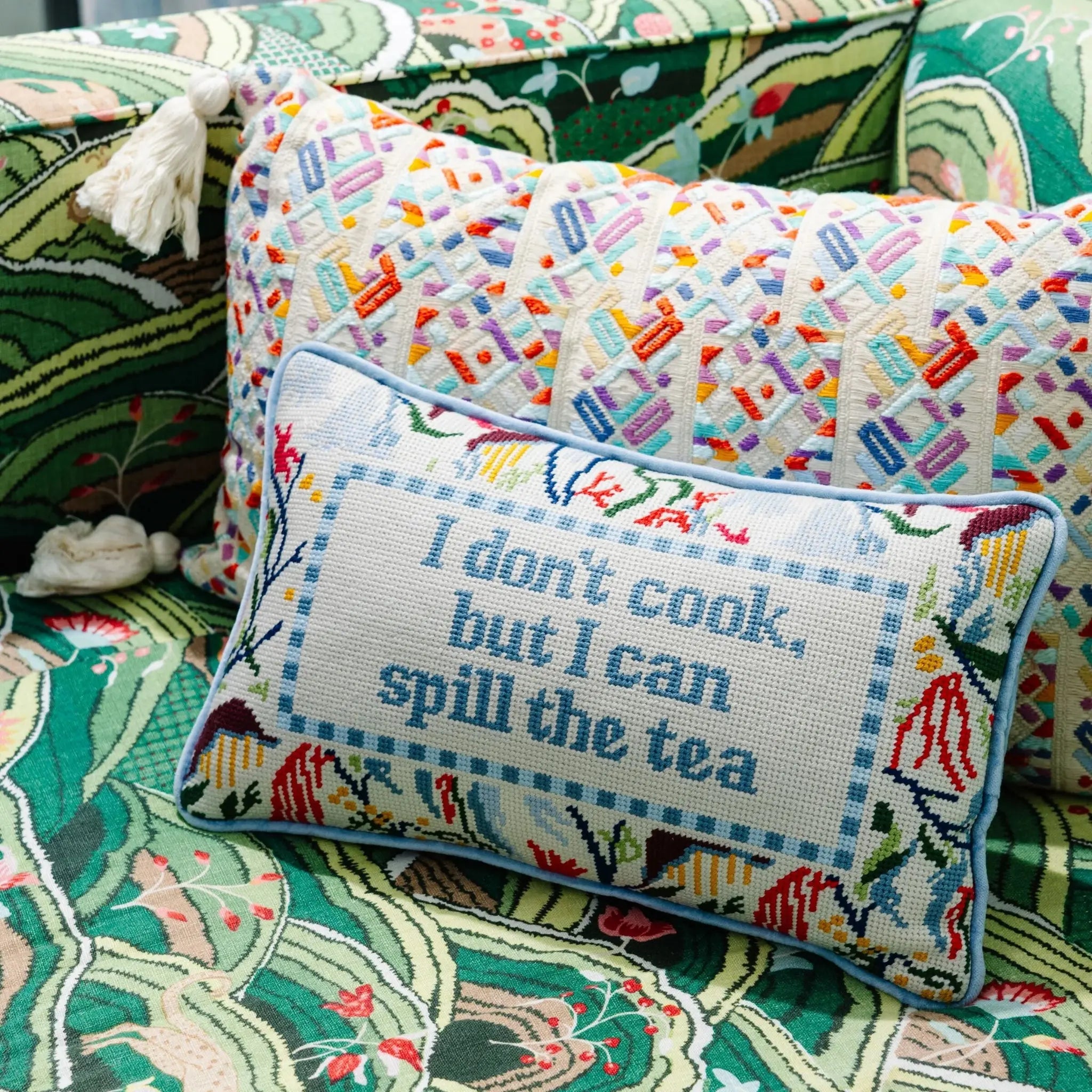 Decorative pillow with colorful cross-stitch pattern and text on a patterned couch.