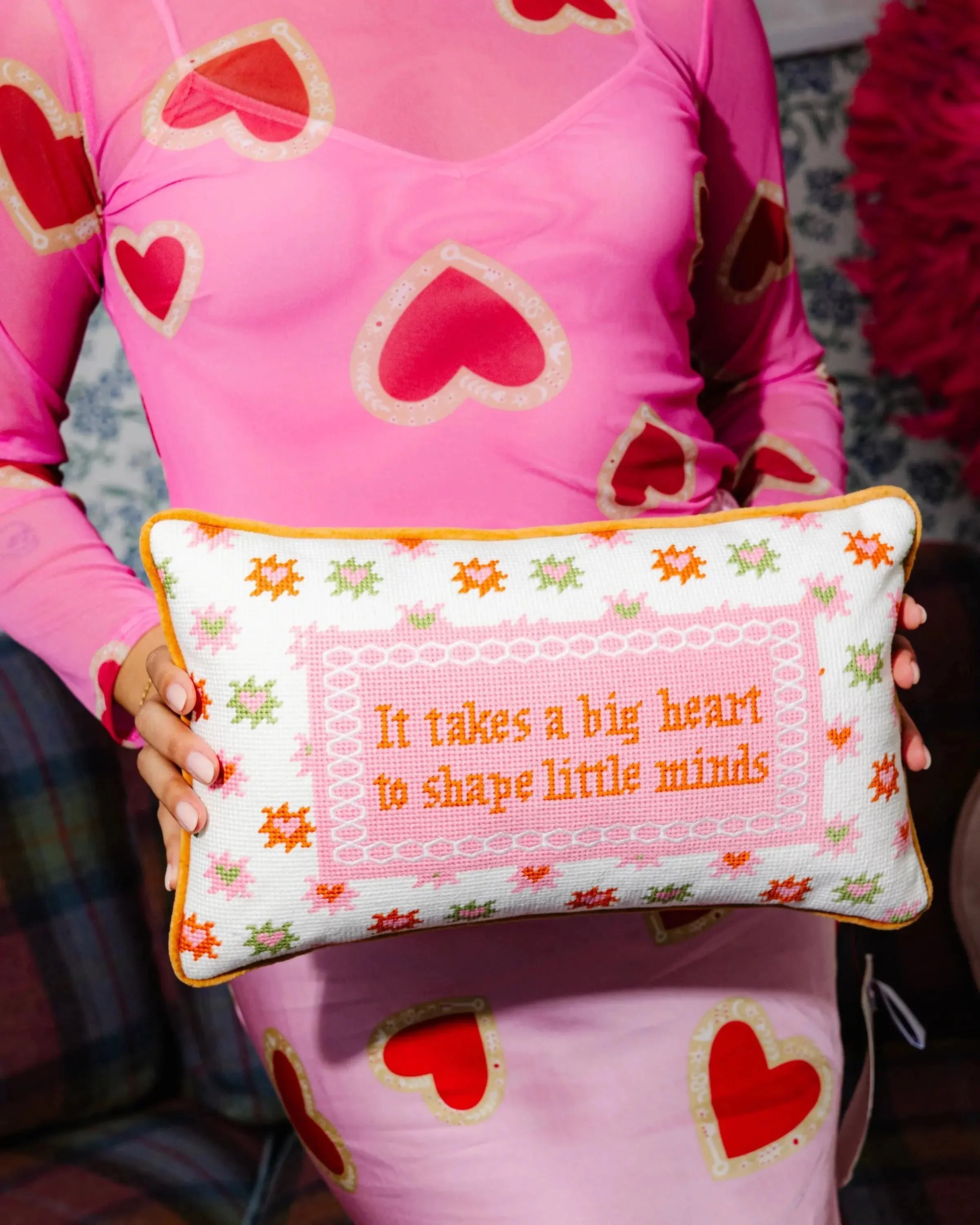 Person wearing a pink outfit with heart patterns holding a decorative pillow with text.