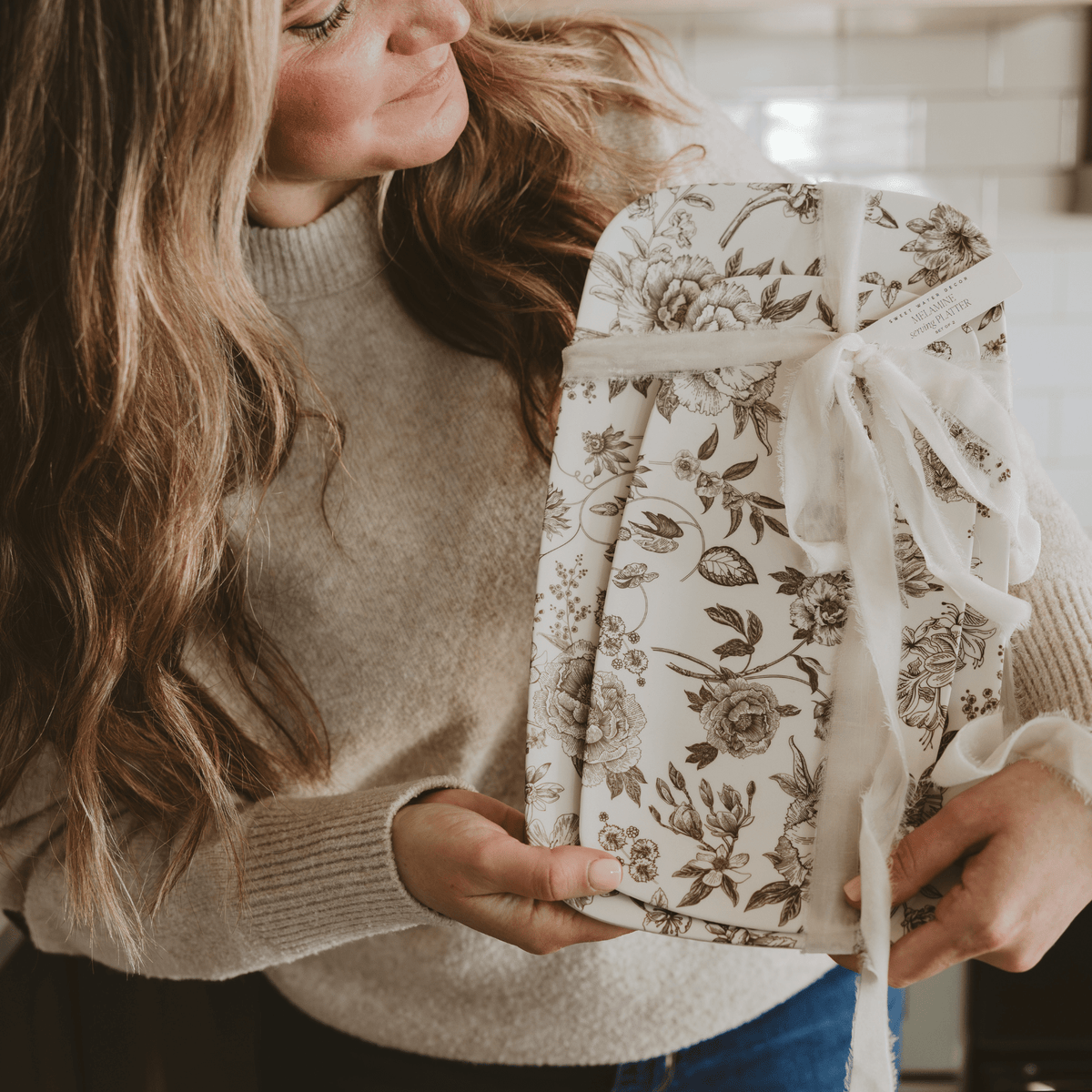 Woman holding a floral-patterned gift box in a kitchen setting
