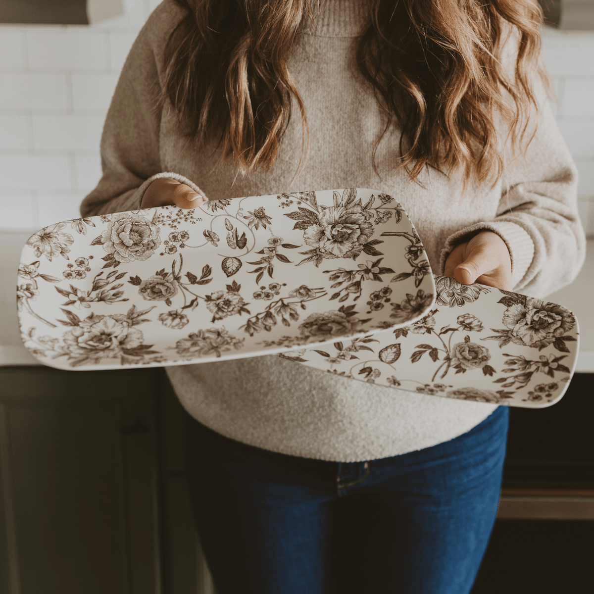 Person holding a floral-patterned tray in a kitchen setting