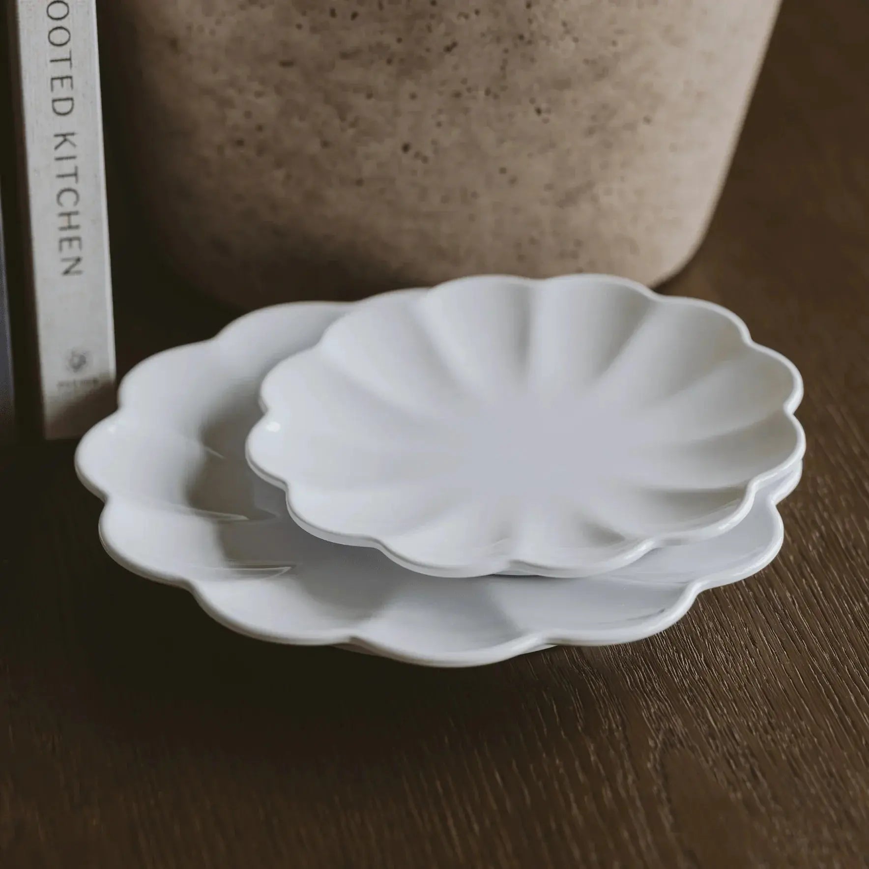White scalloped ceramic plates for farmhouse kitchen decor, styled on wood surface with book and vase