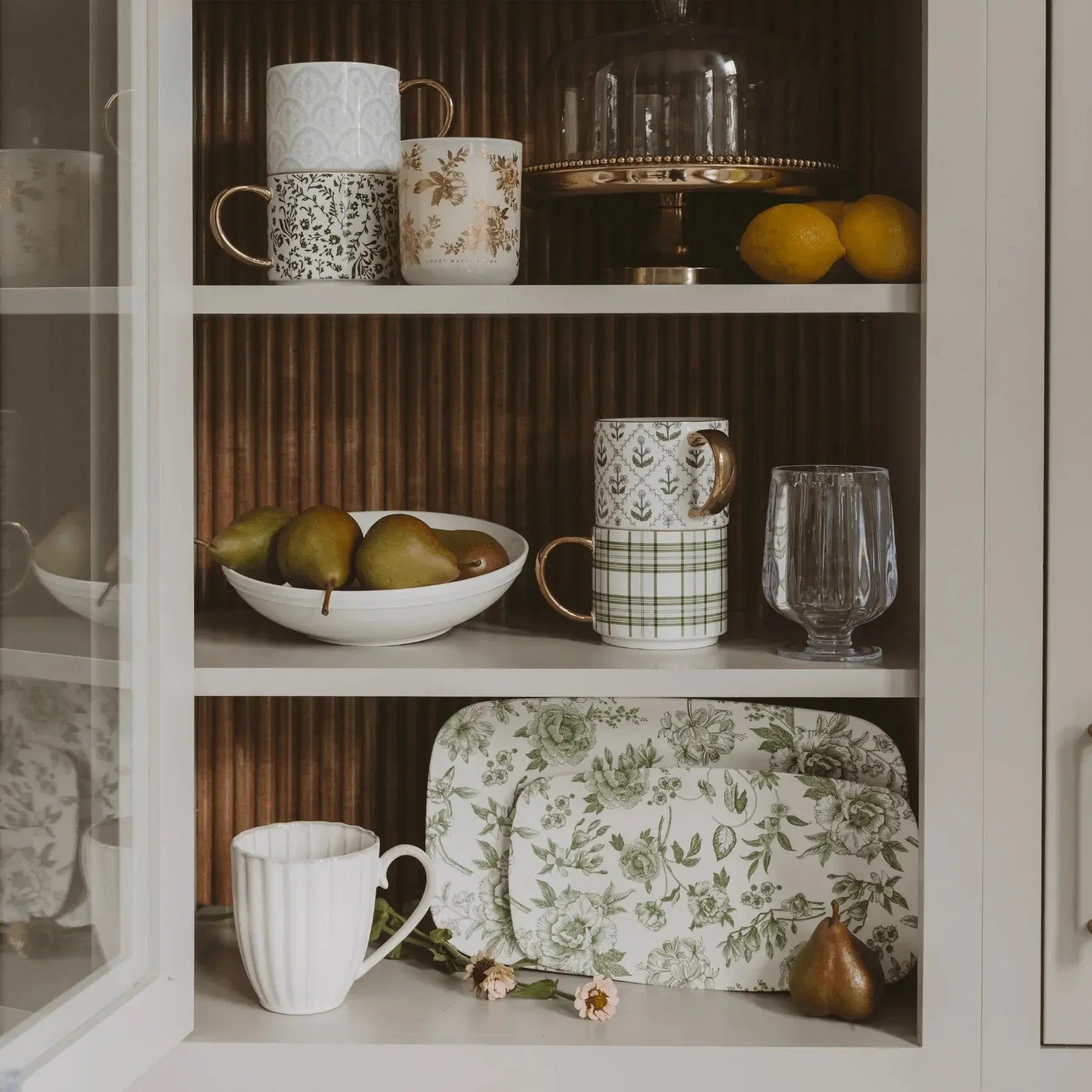 Cozy farmhouse kitchen hutch with floral mugs, green plaid cups, ceramic plates, lemons, and pears for cottage style decor