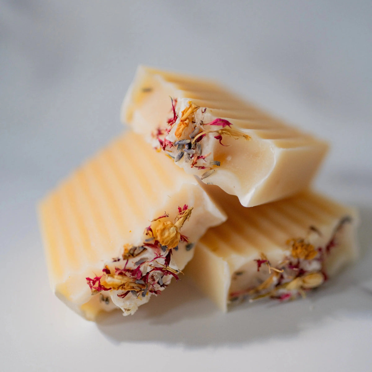 Three pieces of white soap with floral bits on a light gray background