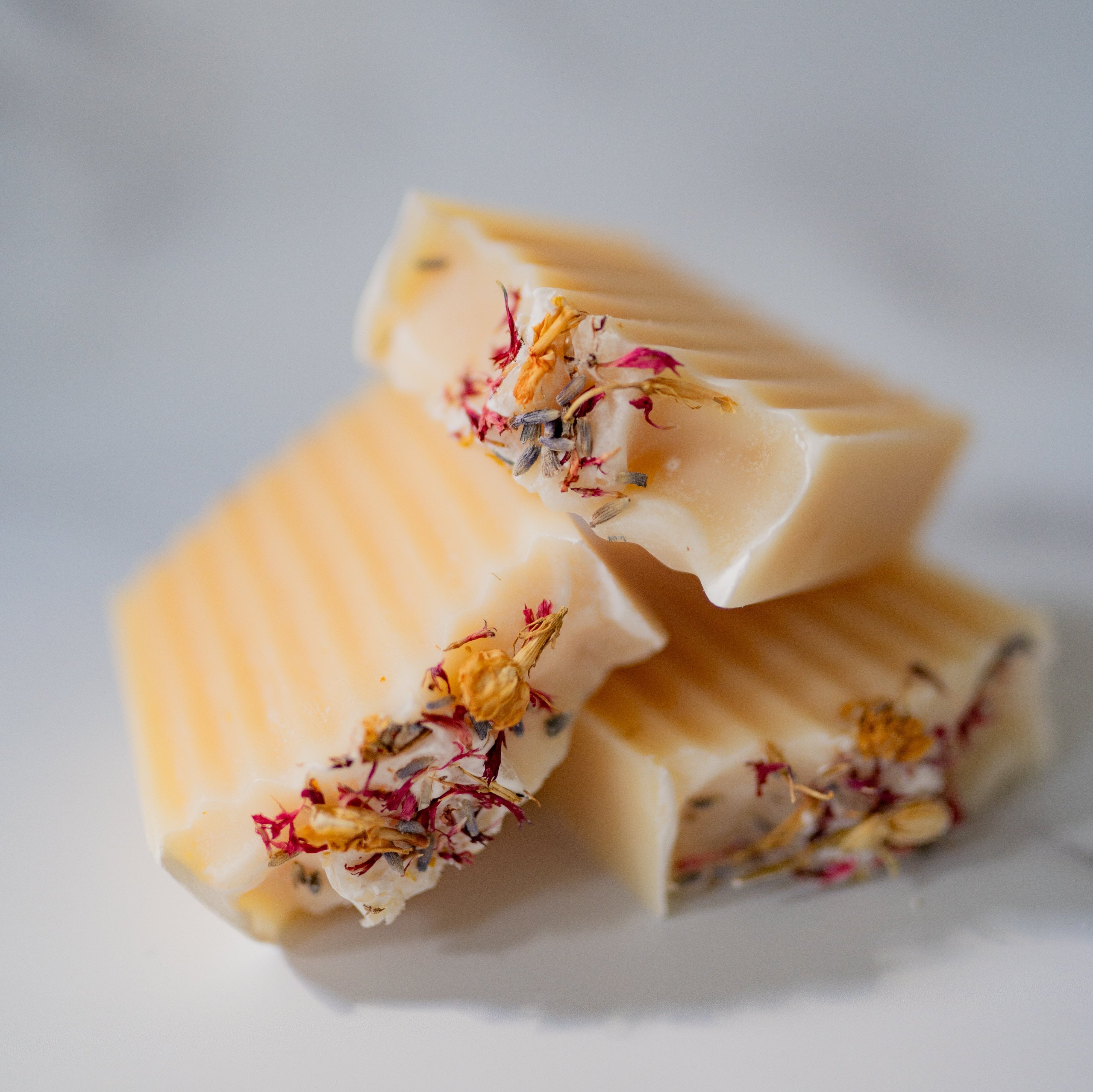 Three pieces of white soap with floral bits on a light gray background