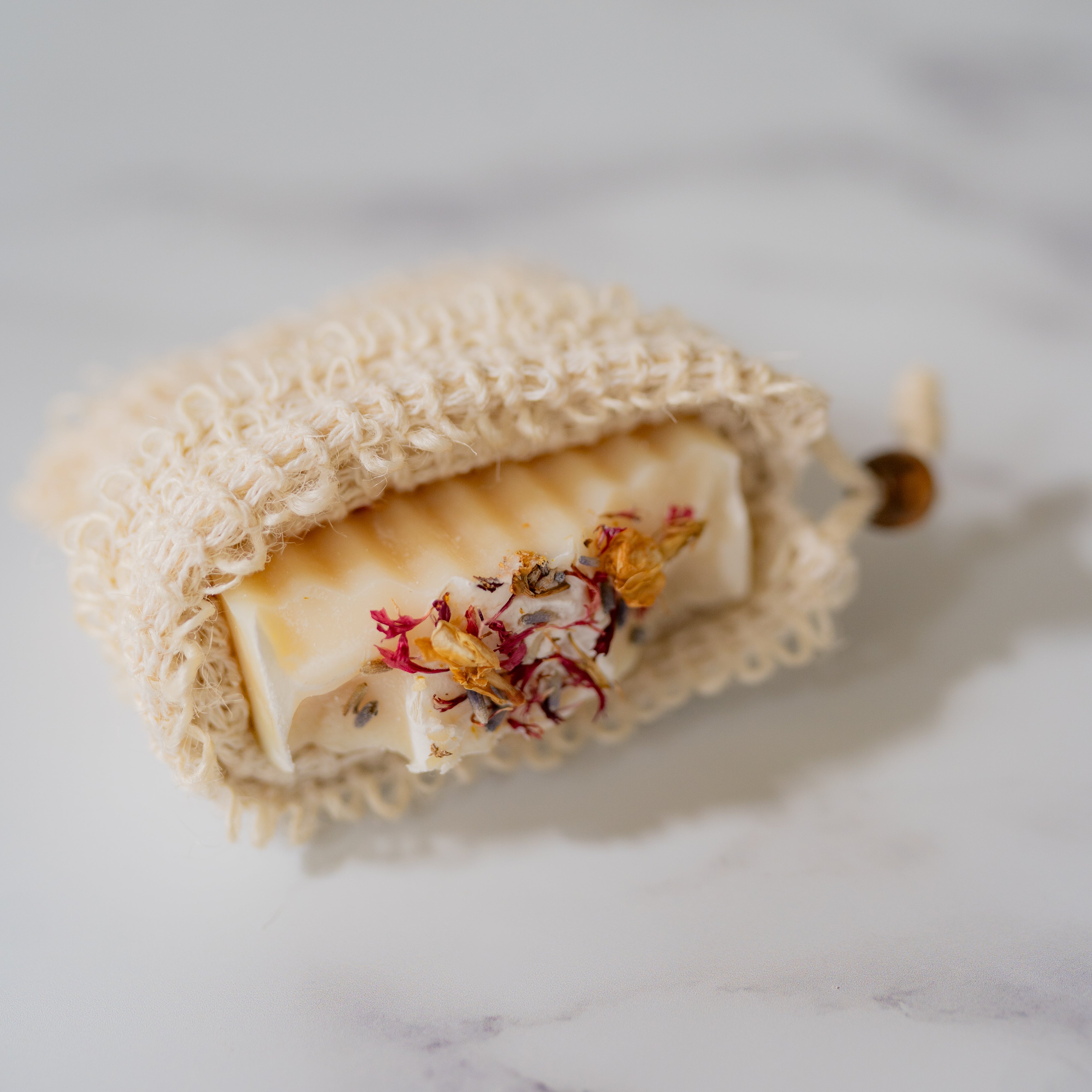 Bar of soap with floral elements in a natural fiber bag on a marble surface