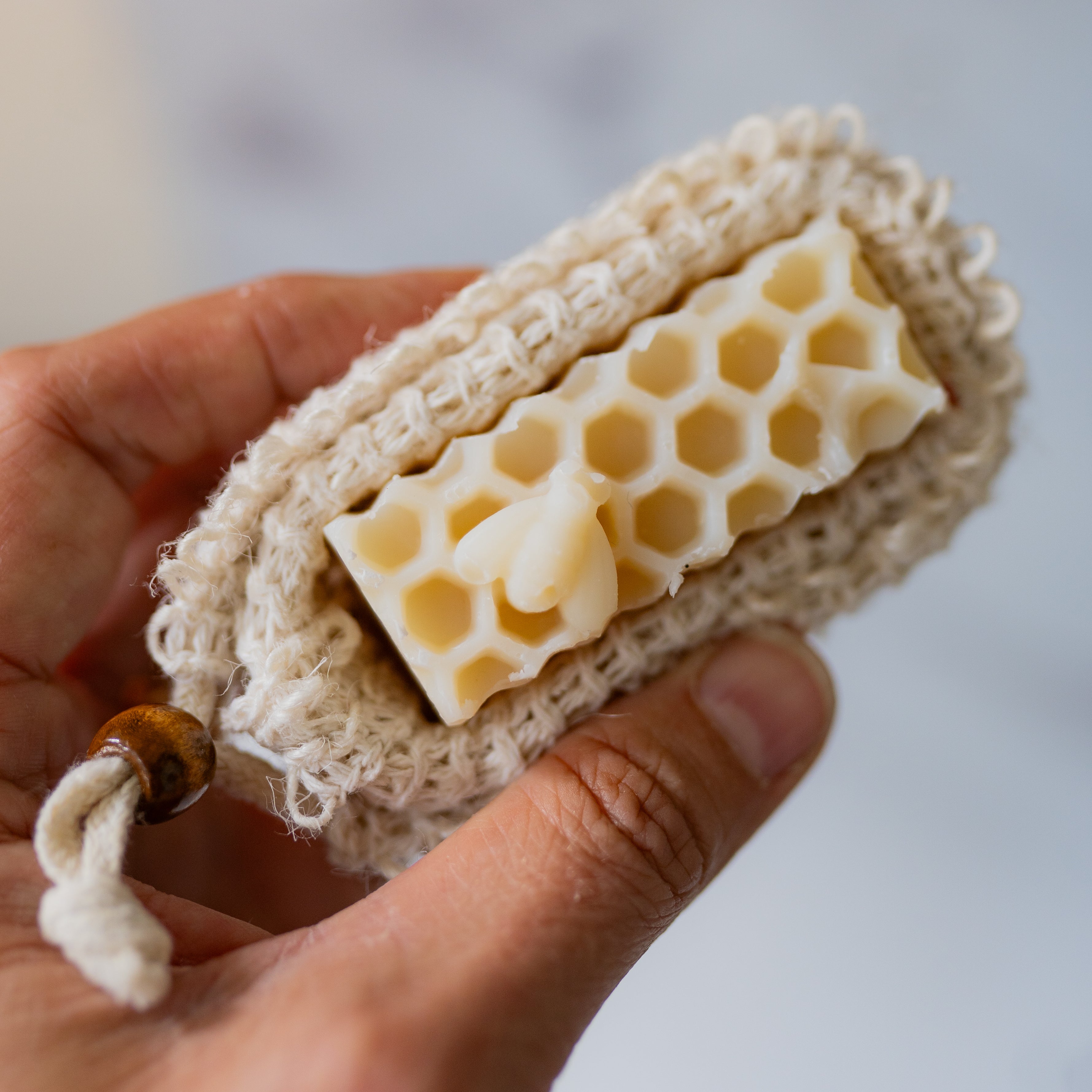Hand holding a bar of soap with honeycomb design on a natural fiber soap bag.