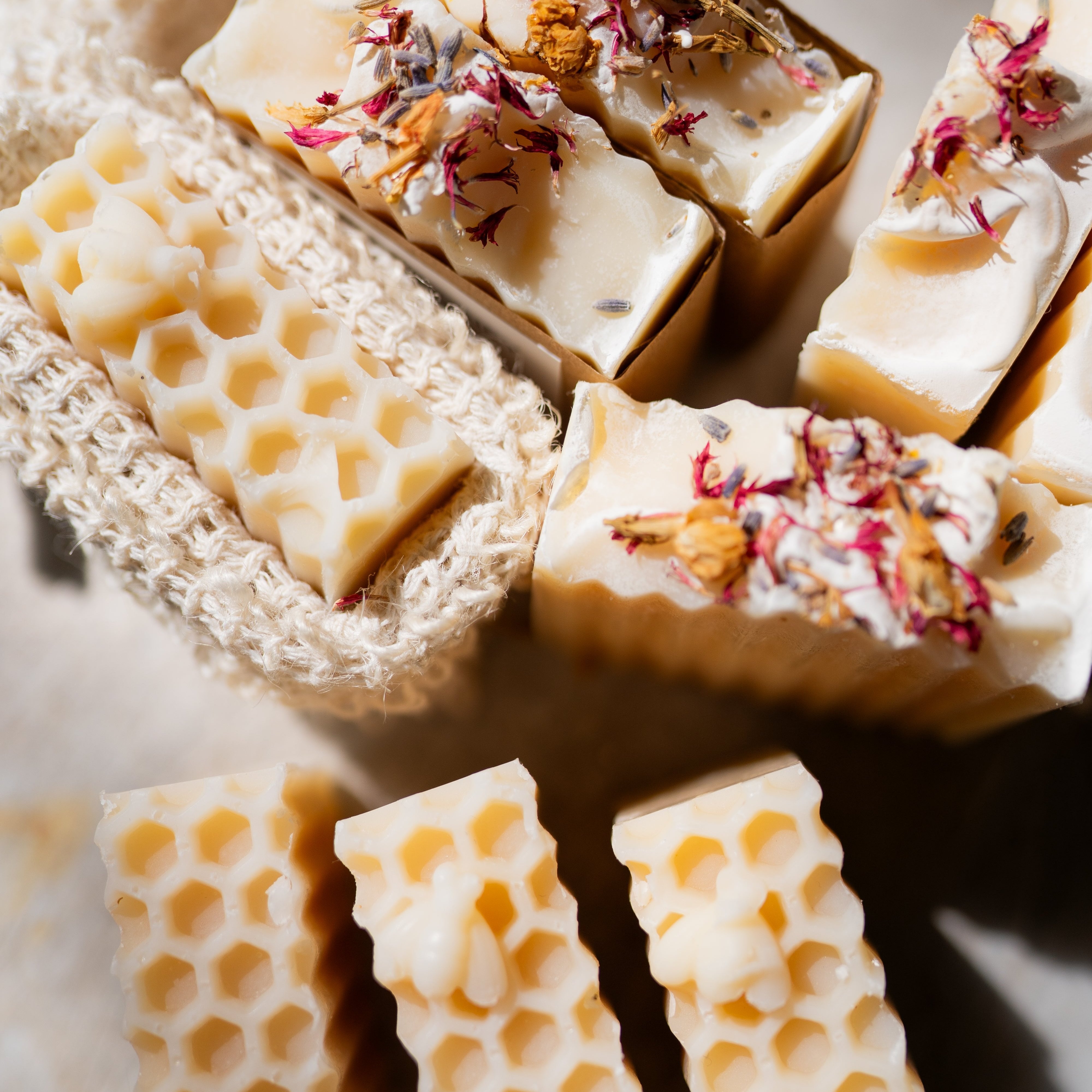 Close-up of handmade honey-colored honeycomb soap bars topped with dried flower petals, arranged on a neutral surface with a knitted soap dish.