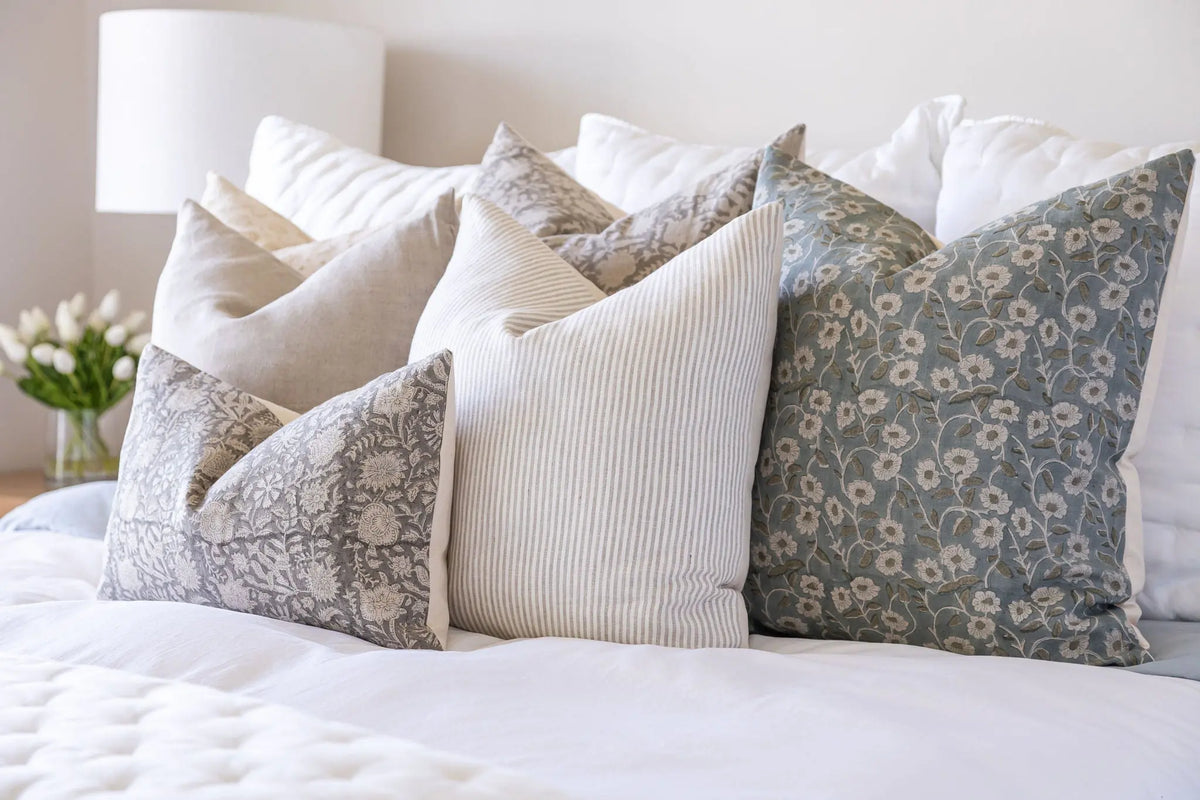 Decorative pillows on a bed with a lamp and flowers in the background
