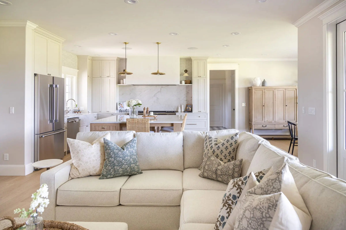 Living room with a beige sectional sofa, decorative pillows, and a kitchen in the background.