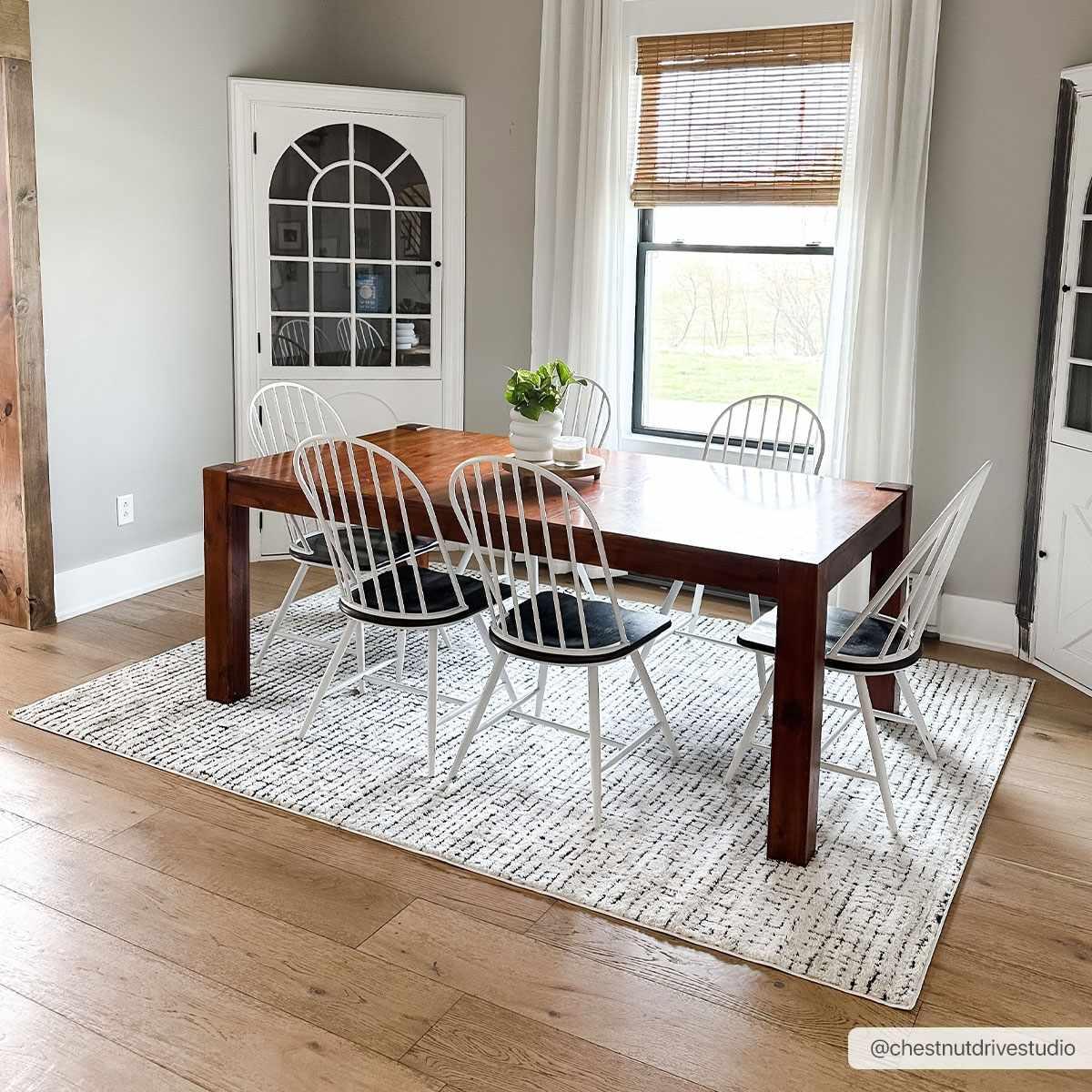 Farmhouse dining room with wooden table, white spindle chairs, and cozy rug for cottage-style home decor
