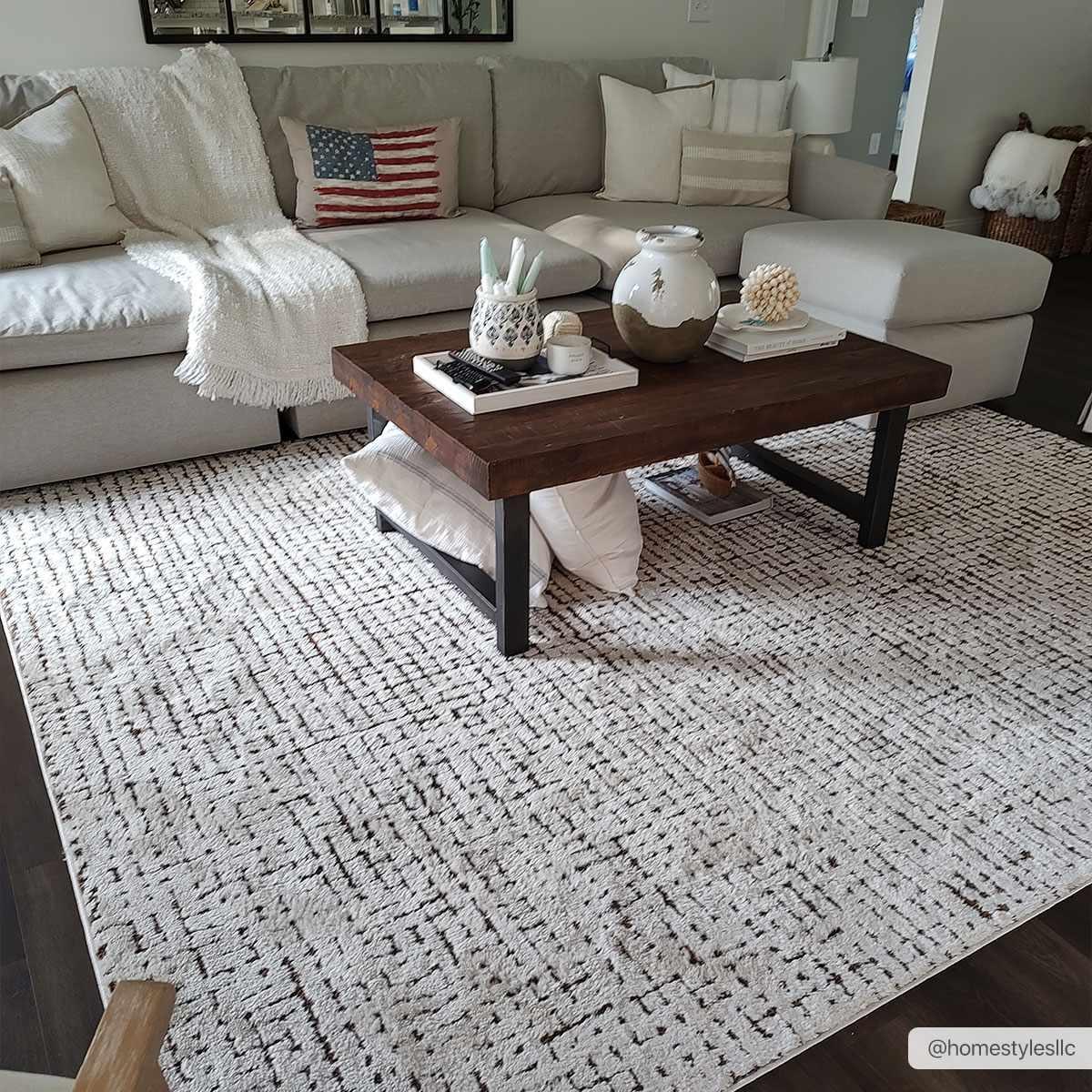 Cozy farmhouse living room with neutral sectional sofa, patterned rug, and rustic coffee table decor