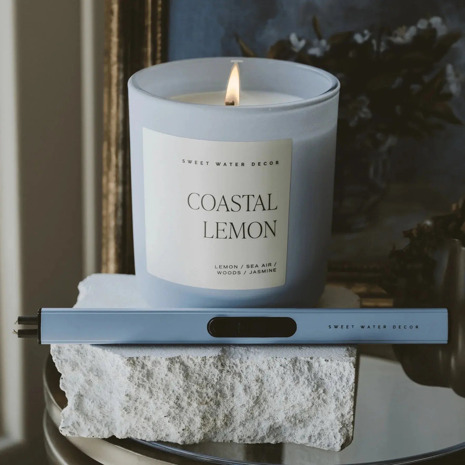 Coastal Lemon scented candle in frosted glass, lit, with matching lighter, styled on stone for cozy home decor